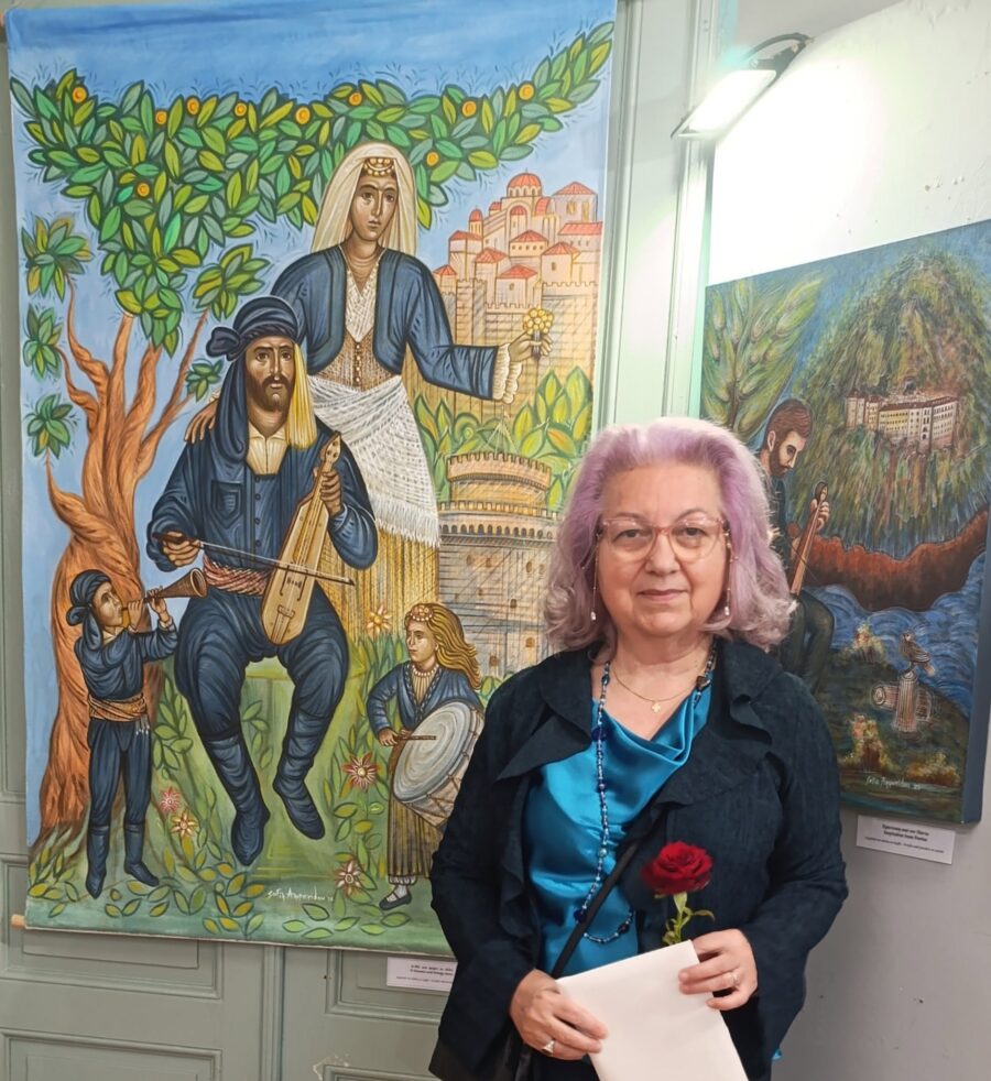Η ζωγράφος Σοφία Αμπερίδου μπροστά σε ζωγραφικά έργα με παραδοσιακές μορφές και μουσικούς.